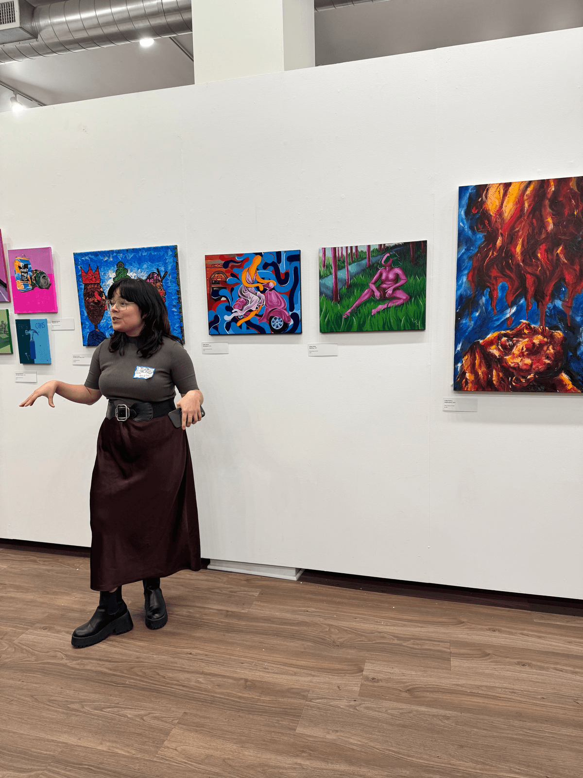 An artist presenting and gesturing toward their paintings on the gallery wall during the artist talk event