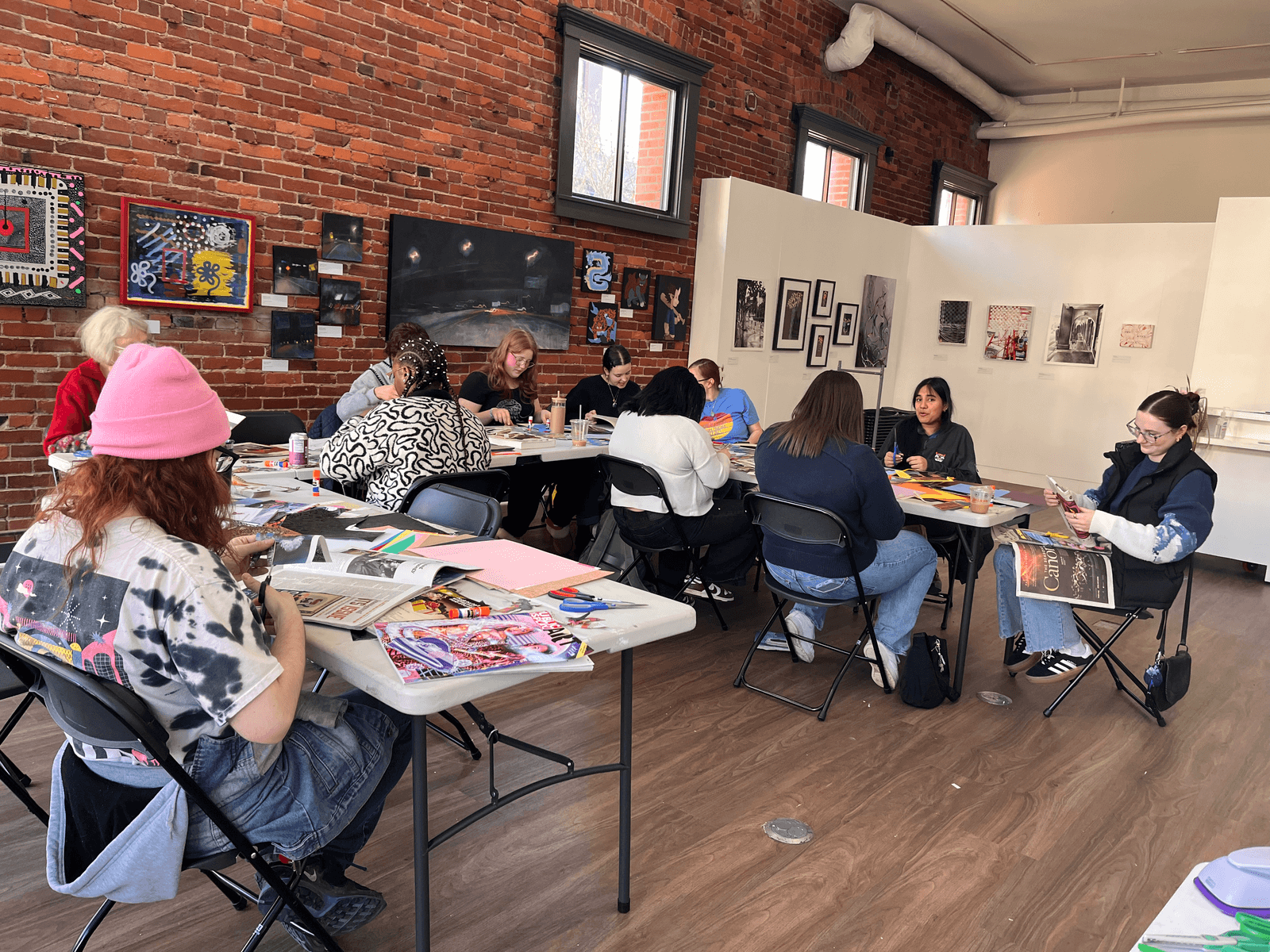 Participants seated at long tables working on collages during the collage workshop, surrounded by art materials and magazine clippings