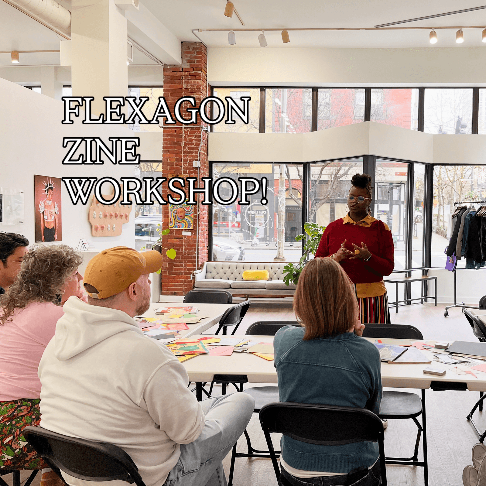 An artist leading the flexagon zine workshop, standing at the head of a table with participants seated around colorful paper materials
