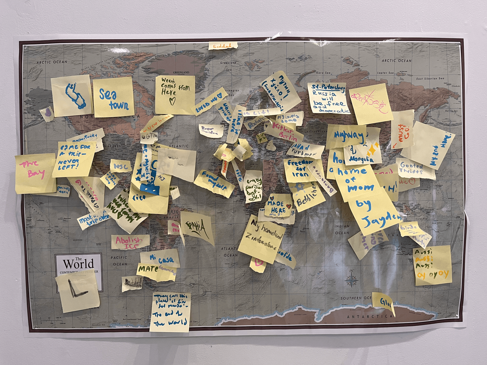 Full view of the interactive world map installation with dozens of sticky notes pinned across different countries and continents