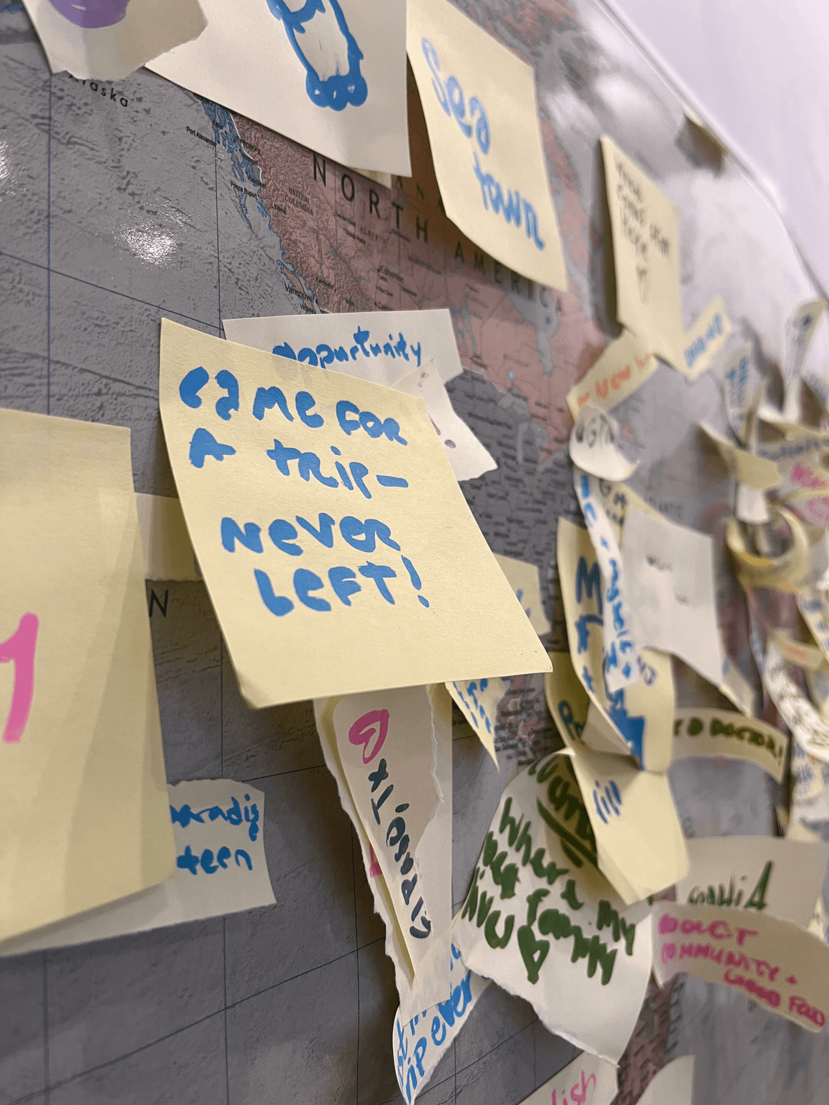 Close-up of the interactive world map covered in sticky notes with handwritten messages from visitors, including 'Came for a trip — never left!'