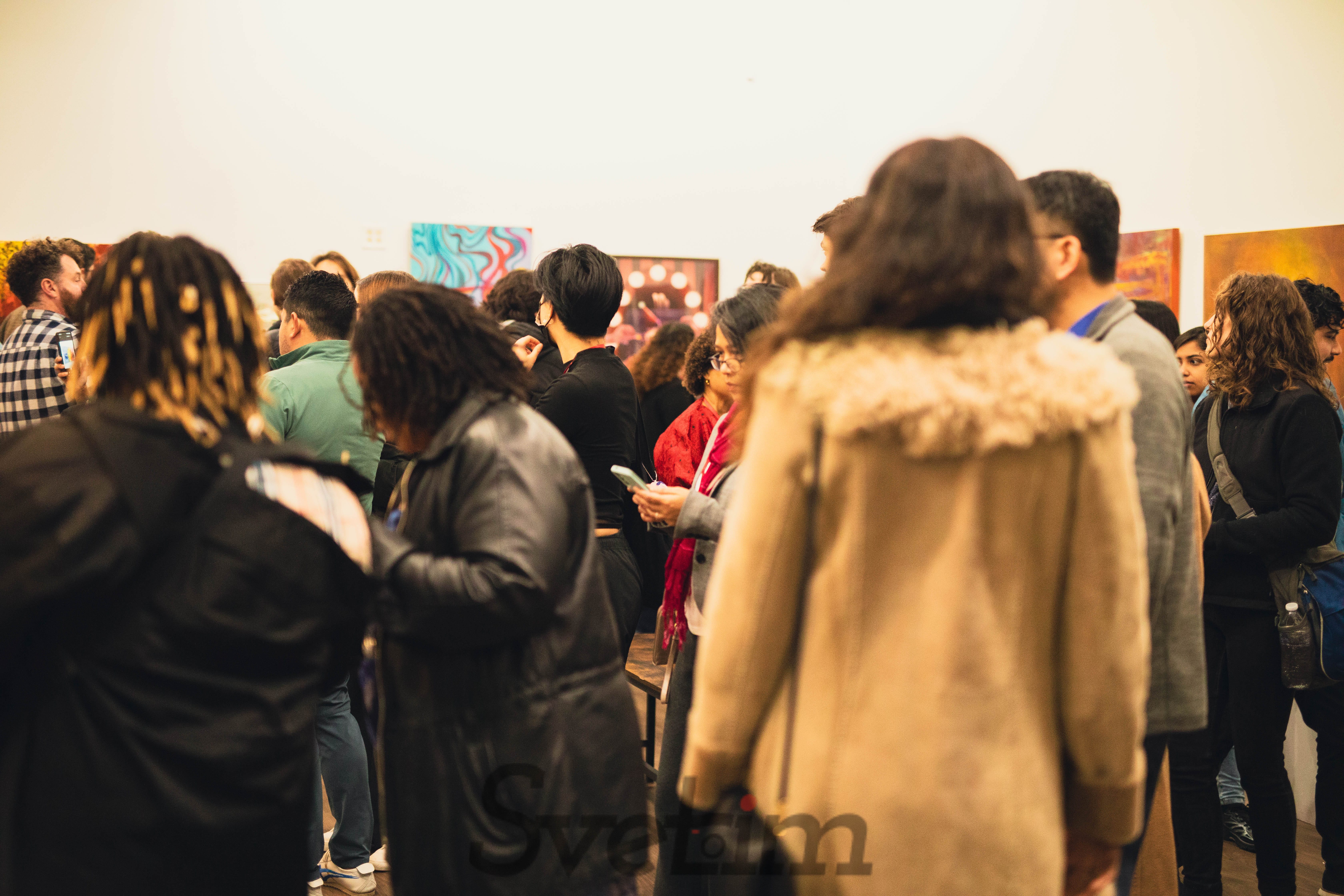 Opening night at Our Light Unbound — the gallery packed with visitors viewing artwork on the walls, artwork ranging from paintings to mixed media installations