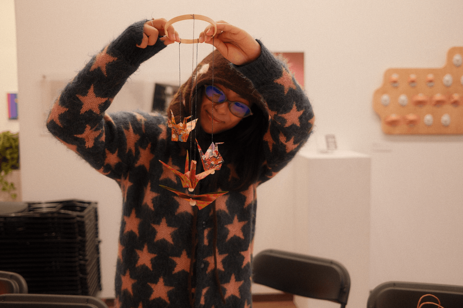 A participant holding up their completed origami crane mobile, smiling proudly at their creation