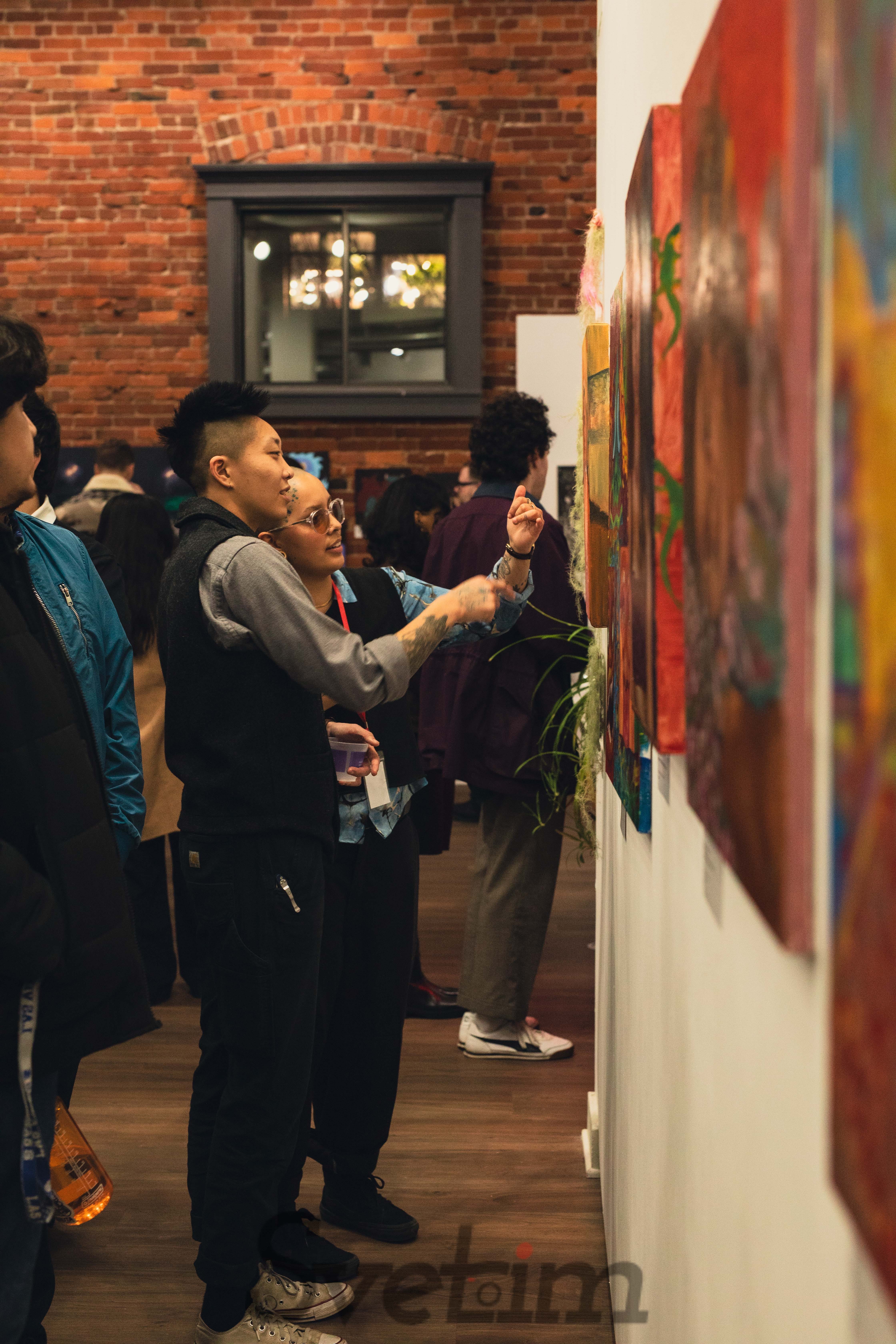 Visitors examining paintings up close at the exhibition, pointing at and discussing the artwork on display